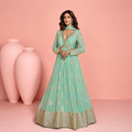 Woman wearing a light green traditional outfit with gold embroidery against a pink background